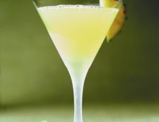 A yellow cocktail in a martini glass garnished with pineapple